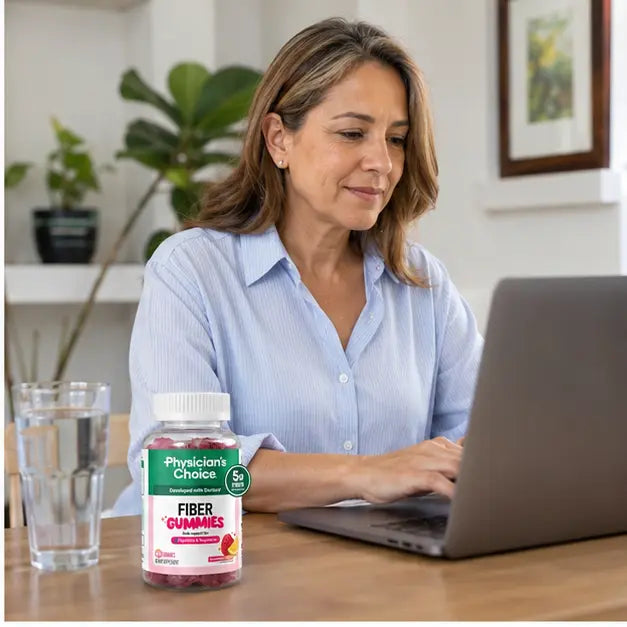 Mujer trabajando con Fiber Gummies y agua junto al computador